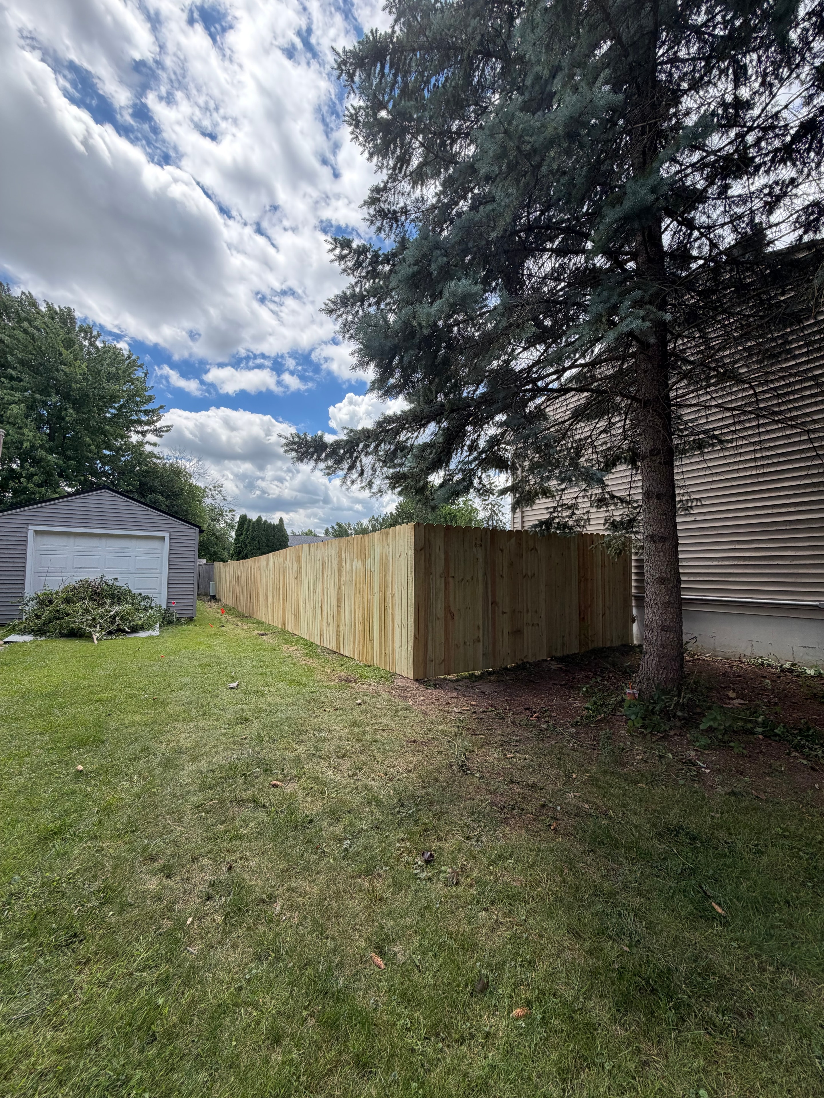 New fence run along yard with pine tree and garage